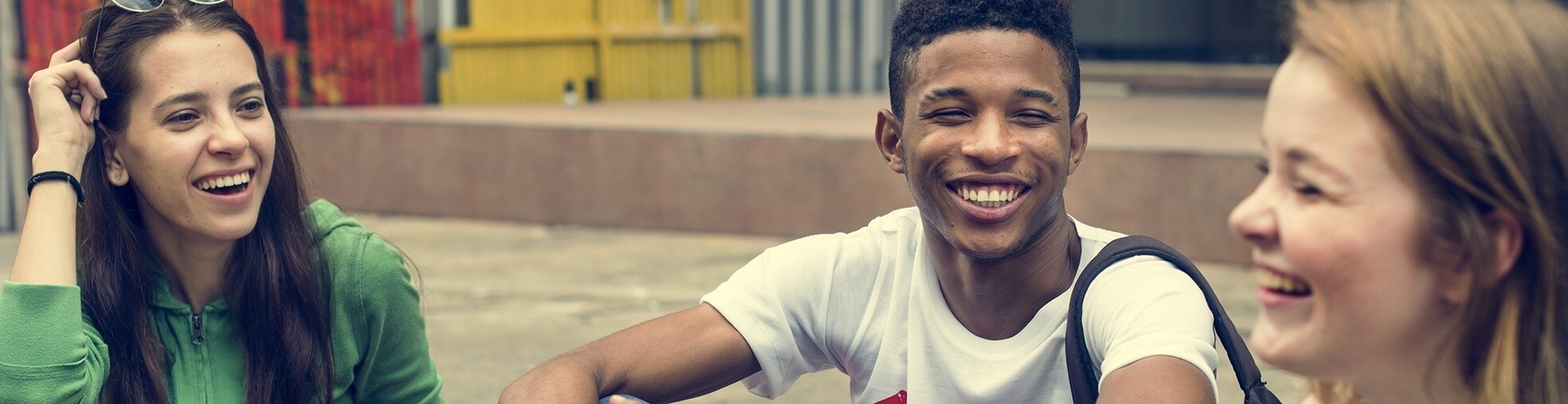 Three young people laughing and talking together in an outdoor setting, sharing a positive social experience.
